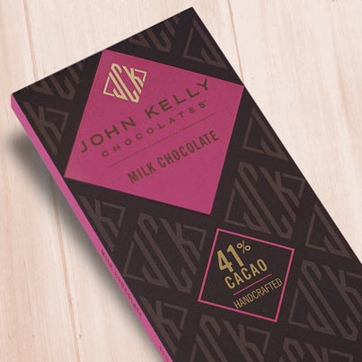 A dark brown, rectangular box. There is a pink diamond on it that holds a John Kelly Chocolates logo and the product name.