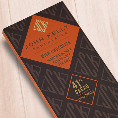A dark brown, rectangular box. There is an orange diamond on it that holds a John Kelly Chocolates logo and the product name.