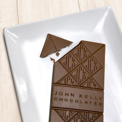 A milk chocolate solid bar with the top left corner cut off from it. The bar has a John Kelly Chocolates logo on it.