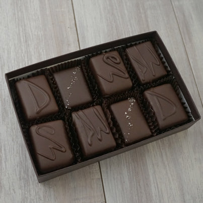 An open box of our eight piece dark assortment. Eight chocolates can be seen neatly sitting in brown, paper cups. They are packed tightly into the brown box.