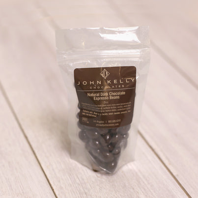 A bad of dark chocolate covered espresso beans sits with a brown label on it. The label features a John Kelly Chocolates logo.