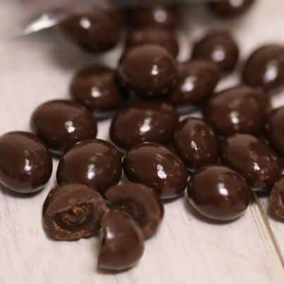 Dark chocolate covered espresso beans are laying out with a few cut in half.