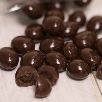 Dark chocolate covered espresso beans are laying out with a few cut in half.