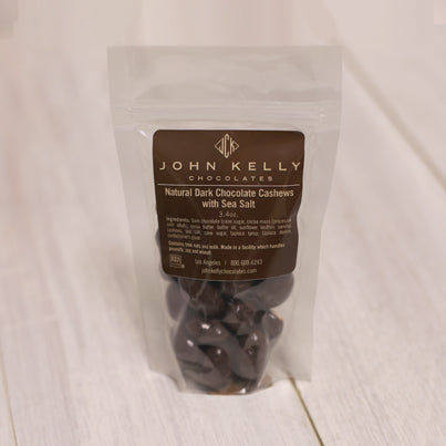 A bag of chocolate covered cashews stands. The label on the bag is brown and features a John Kelly Chocolates logo.