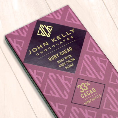 A pink ruby chocolate bar box. The box has the John Kelly Chocolates logo all over it in pink and has a purple label that states what the product is.