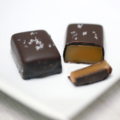 Two fleur de sel salted caramels sit on a plate. One is cut open revealing the gooey caramel inside.