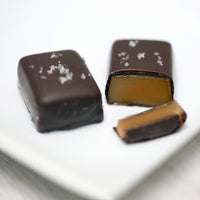 Two fleur de sel salted caramels sit on a plate. One is cut open revealing the gooey caramel inside.