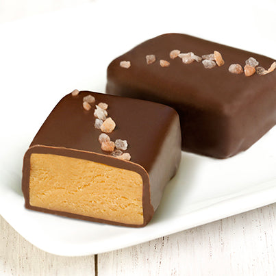 Two pink salted truffle fudge bites. One is cut in half to reveal the peanut butter inside.