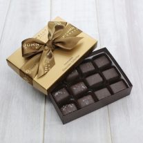 An open salted caramel gift box. The lid is partially on the box and is tied with a John Kelly Chocolates ribbon.