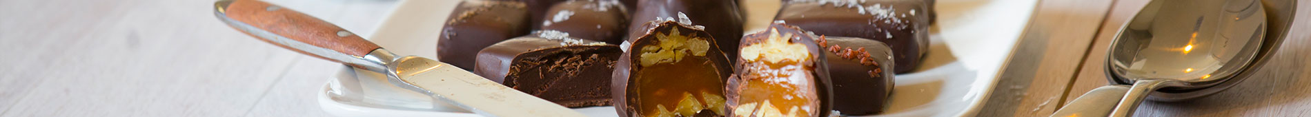 Chocolate on a plate. Some are cut in half and sitting next to a knife. To the right of that is two silver spoons stacked on top of each other.