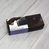 A rectangular, dark brown box with a white chocolate and peanut butter sleeve on it. The box has a brown ribbon on it.