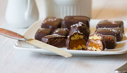 Multiple chocolates on a plate. Some are cut open to reveal a gooey caramel inside. A knife sits on the corner of the plate.