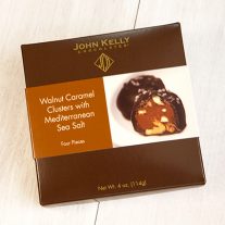 A closed four piece salted walnut caramel cluster box. The box is a dark brown with a sleeve on it with a picture of the chocolate.