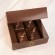 Four chocolates sit in a dark, brown box. They all have pinkish salt going diagonally across them.