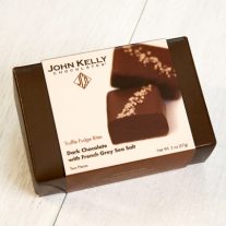A dark brown box with a white sleeve on it. The sleeve features an image of two grey salted truffle fudge bites on it.
