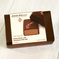 A dark brown box with a white sleeve. The white sleeve has an image of two pink salted truffle fudge bites on it as well as a brown John Kelly Chocolates logo on it.