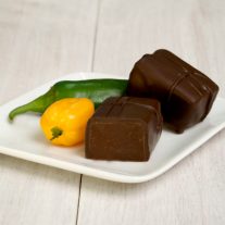 Two habanero chocolate bars on a plate. One of them is cut open revealing the chocolate inside. Two jalapenos sit next to the bars.