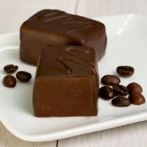 Two dark chocolate espresso bars sit on a plate. They are surrounded by espresso beans.