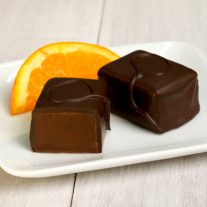 Two orange flavored chocolate bars sit on a plate. An orange slice sits behind them.