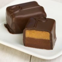 Two chocolate bars on a white plate. One is cut open to reveal a layer of peanut butter and chocolate within the chocolate bar.