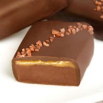 A piece of chocolate with redish salt on top. It is cut in half to reveal a layer of caramel and chocolate.