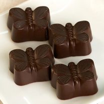 Four dark chocolate butterflies on a white plate.
