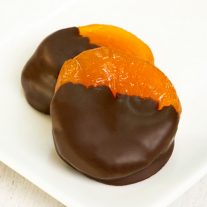 Two chocolate dipped apricots on a plate.