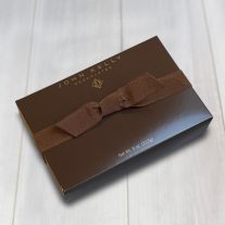 A closed 8 piece assortment box with a brown ribbon. The box is brown and has a John Kelly Chocolates logo written in gold.