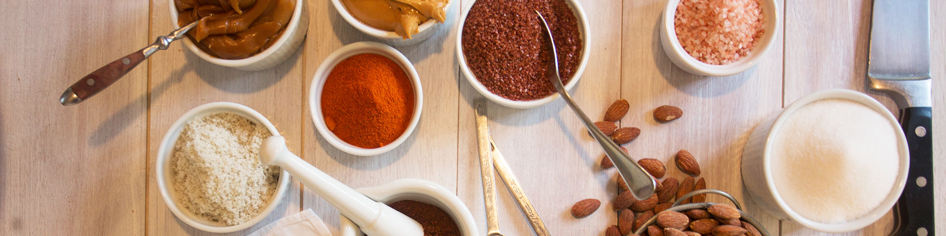 Various salts, spices, and nuts in white bowls.