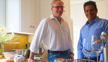 John Kelson and Kelly Green standing in a kitchen. Kelly on the left is wearing a white button down. John on the right is wearing a light blue button down.