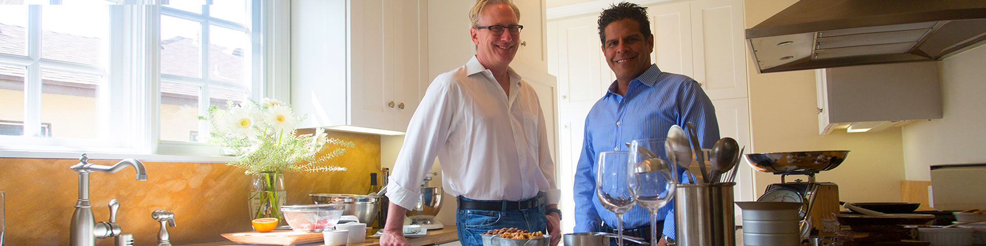 John Kelson and Kelly Green standing in a kitchen. Kelly on the left is wearing a white button down. John on the right is wearing a light blue button down.