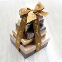 Five boxes are stacked vertically from largest to smallest. They are tied together with a brown bow that has John Kelly Chocolates written on it.