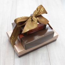 Three boxes stacked vertically from largest to smallest. They are tied together with a brown bow that reads John Kelly Chocolates.