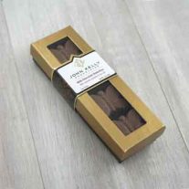 A closed four piece milk butterfly box. The box is a long rectangle shape and had a gold lid with a window. Through the window the milk chocolate butterflies can be seen. A label sits about three quarters of the way up the box. It is white and has a John Kelly Chocolates logo on it.