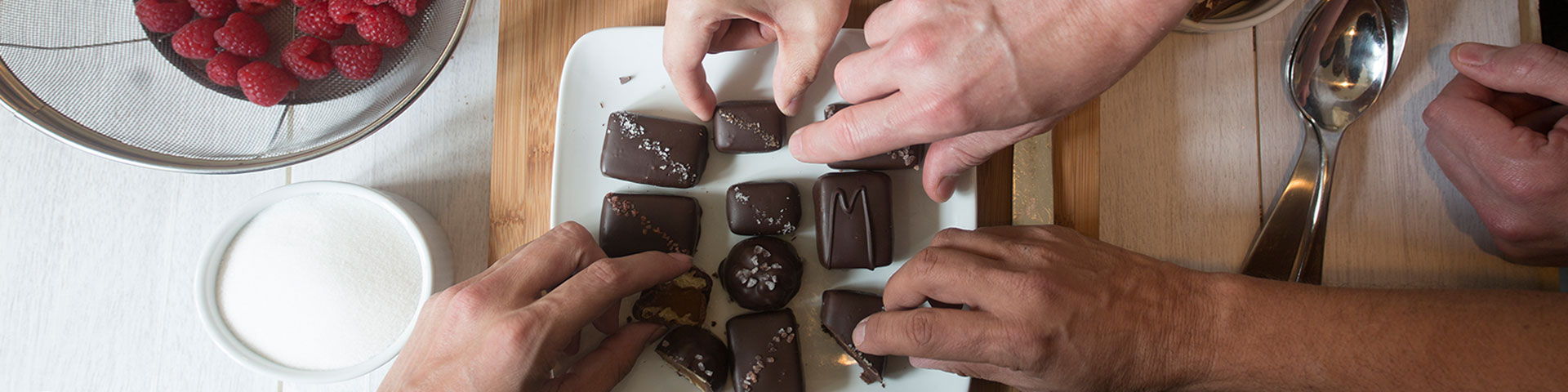Hands are surrounding a delicious plate of chocolates. Some of the hands are holding a piece.