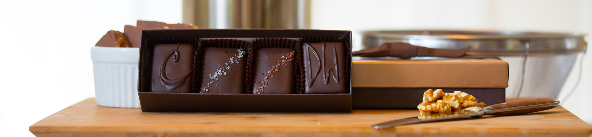 An open four piece assortment box sits open. Next to the box is a closed box with a walnut in front of it.
