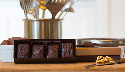 An open four piece assortment box sits open. Next to the box is a closed box with a walnut in front of it.