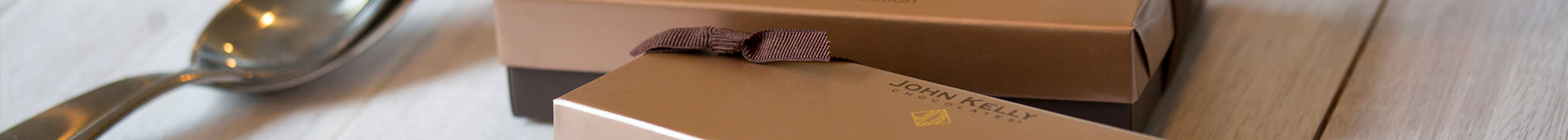 A banner of two chocolate boxes with brown stretch ribbon next to a silver spoon.