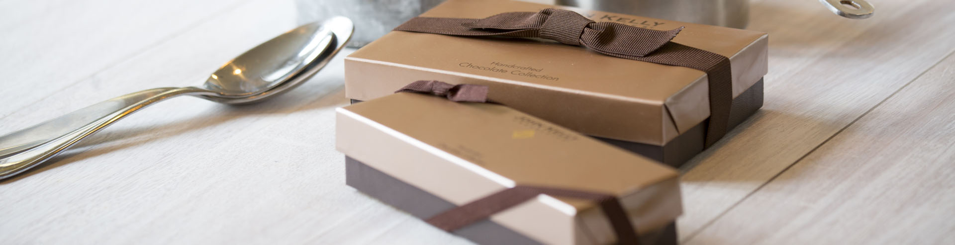 Two boxes with brown ribbon on them. A spoon sits off to the left of the boxes.