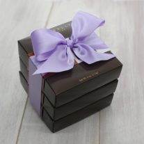 Three dark brown four piece boxes stacked. They are tied together with an orchid ribbon.