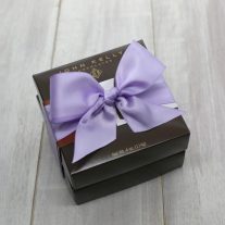 Two dark brown four piece boxes stacked. They are tied together by an orchid ribbon.