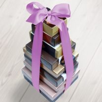 Eight boxes stacked vertically from largest to smallest. They are tied together with an orchid colored ribbon.