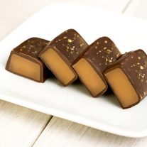 Four applewood smoked salted caramels on a white plate. The gooey caramel inside can be seen in all of them.