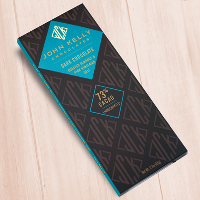 A dark brown, rectangular box. There is a light blue diamond on it that holds a John Kelly Chocolates logo and the product name.