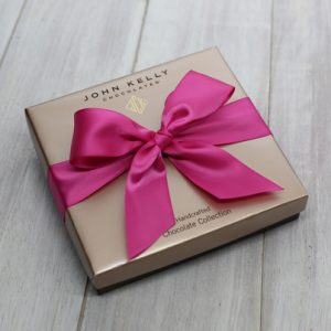 A closed 12 piece assortment box. A large fuchsia ribbon is tied on the top