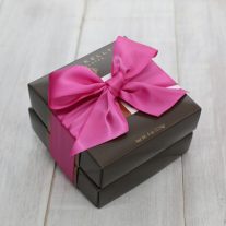 Two brown boxes are stacked on top of each other and tied with a fuchsia ribbon