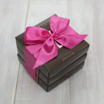 Three dark brown boxes are stacked and tied all together with a fuchsia ribbon