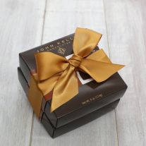 Two dark brown boxes stacked. They are tied together with a gold ribbon.