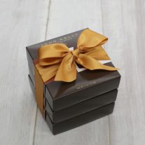 Three dark brown boxes stacked. They are tied together with a gold ribbon.