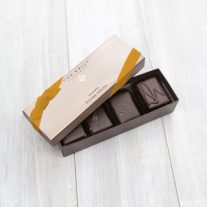 An open 4 piece assortment box with 4 different chocolates from the assortment showing with a gold ribbon on the lid